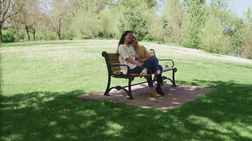 Two women sit together on the park bench