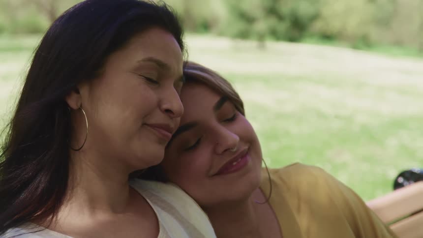 Two women sit together resting on a park bench