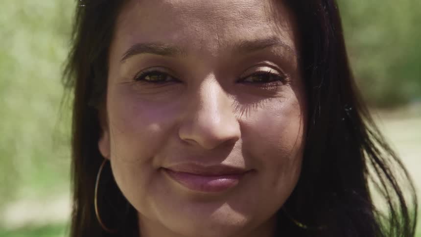 Brunette woman with straight dark hair and earrings stares at the camera