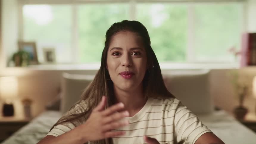 Brunette woman with brown straight hair and a white t shirt talks to the camera
