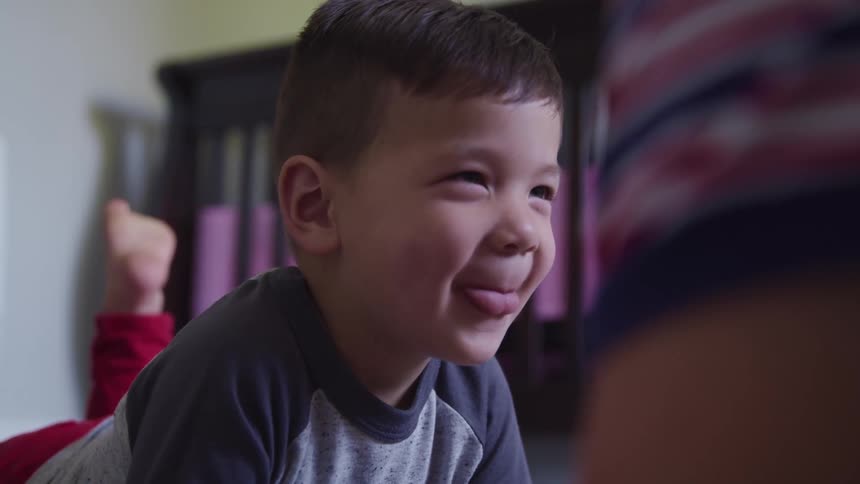A young boy is laying on his stomach while he smiles and laughs very joyfully