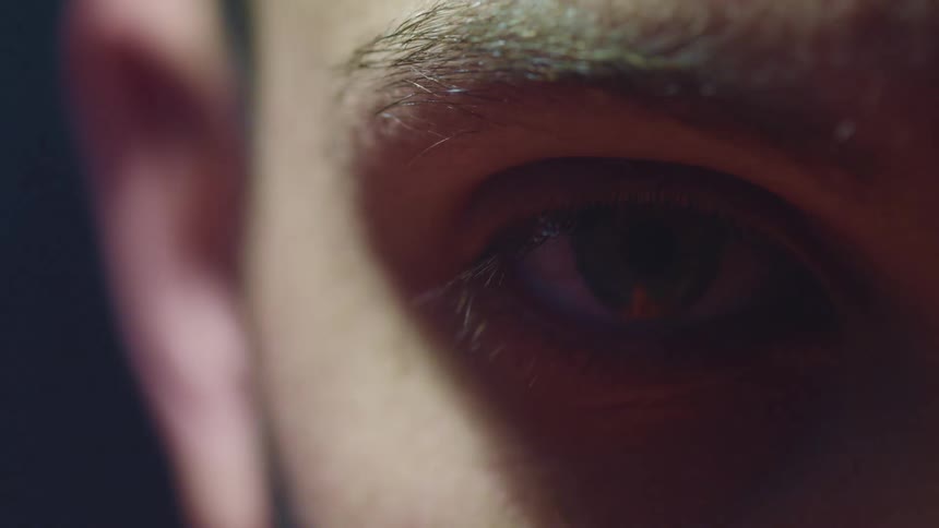 Close up of a young man eye under a swinging white light on a dark room