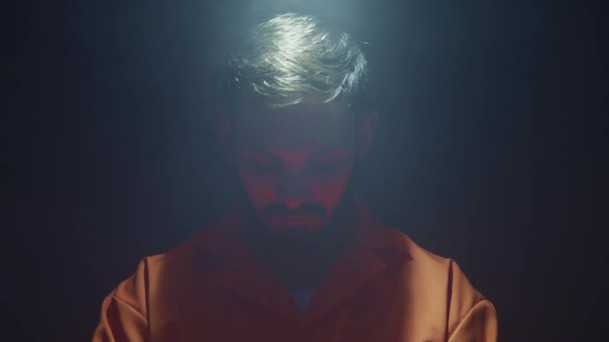 Inmate wearing orangelit by overhead light in smoky dark room