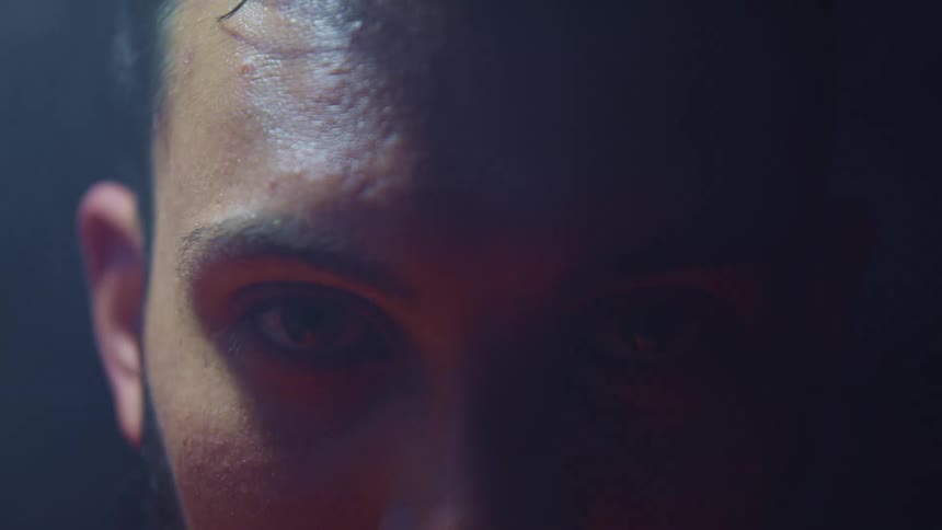 Man stands glaring in dark occasionally lit by moving spotlight