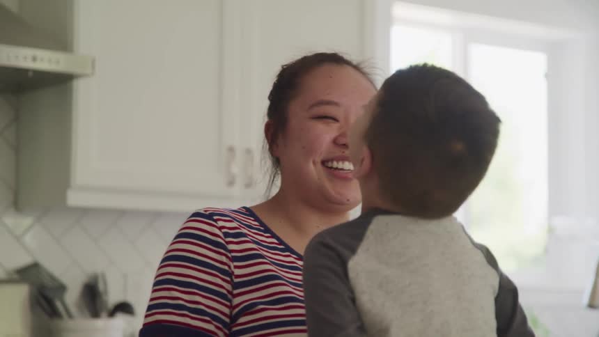 A mother talks and laughs with her young son who is sitting on a kitchen counter