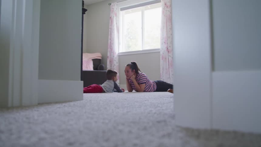 Mother and son talk while laying on the white carpet in the bedroom at home