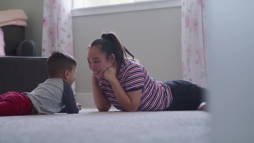 A mother and her son lie on the floor at home and laugh and play