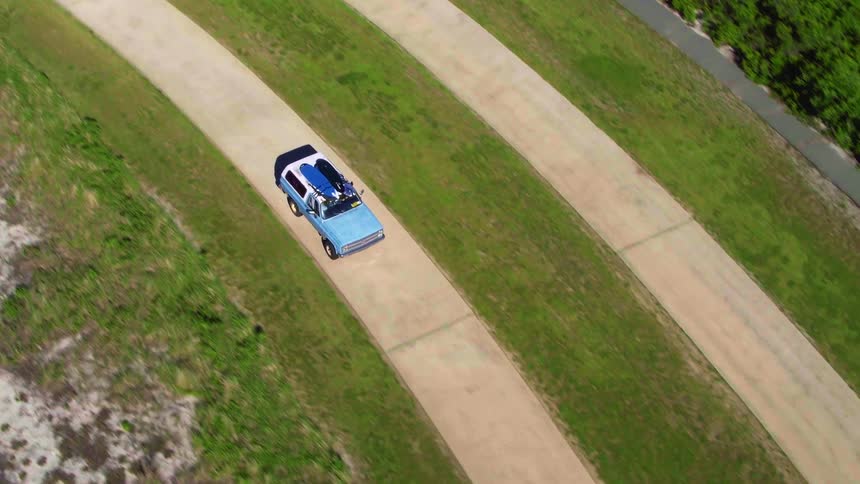 A vehicle with kayaks on the roof drives down a road
