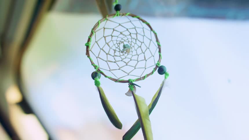 Dream catcher sways back and forth as it hangs from the rearview mirror in a vehicle