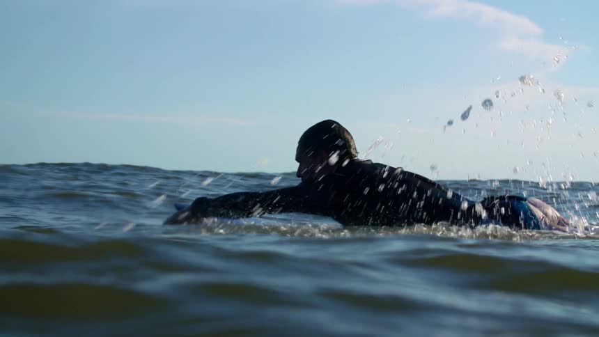 A man paddles a surfboard through the ocean water