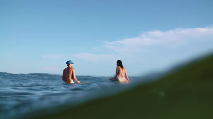 A man and woman sit on a surfboard in the middle of the ocean away from the coast