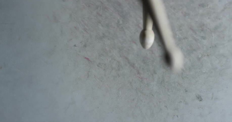 Two drumsticks lightly strike a drum