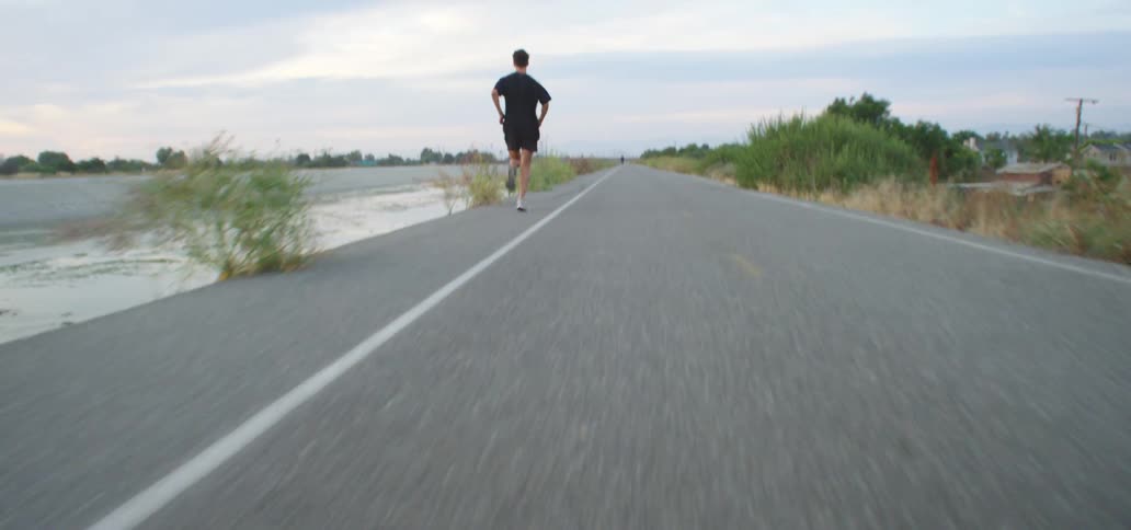 A man is jogging on a road by the ocean coast