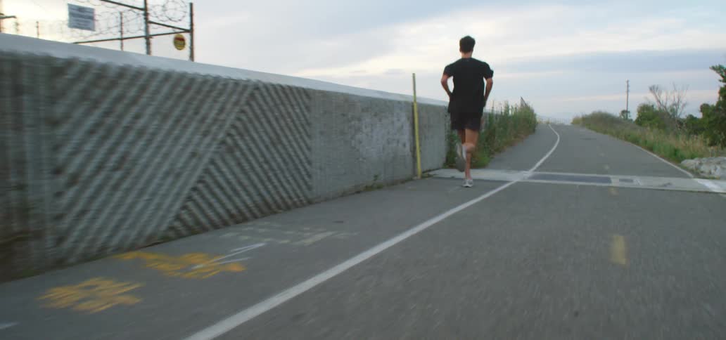 Man with a pair of white shoes black running shorts and a t shirt runs along an asphalt road on a cloudy day