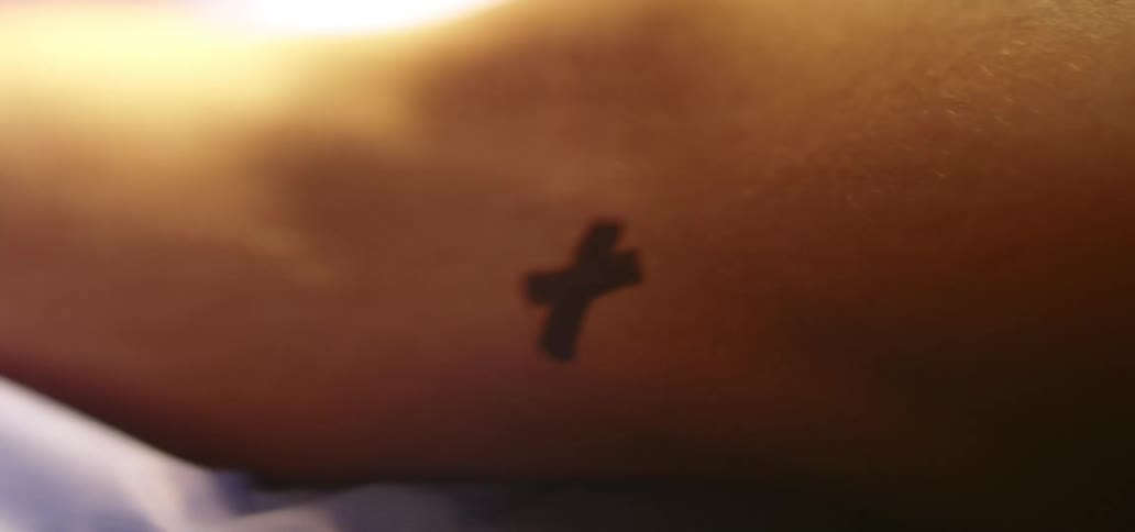 The person has a small cross tattoo on their arm