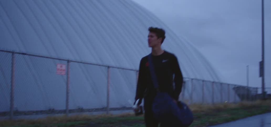 A teenager with a duffle bag on his shoulder walks down the sidewalk next to a large domed building