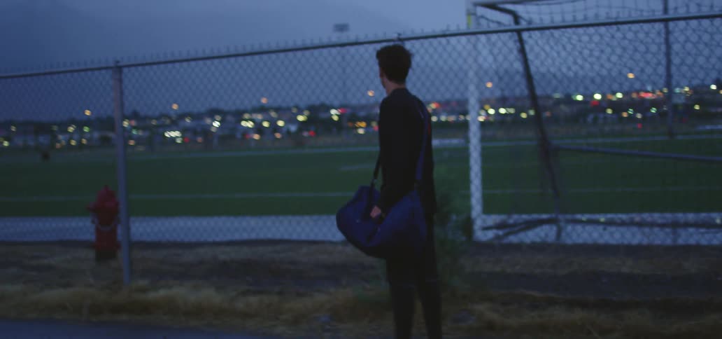 A young man limps past a sports field at light