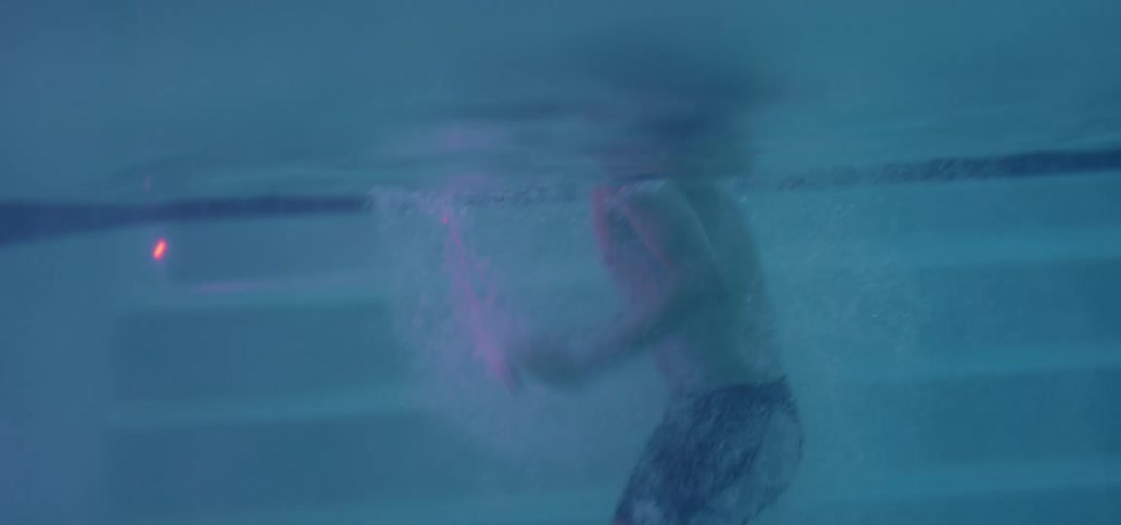 A guy is swimming in a pool at dusk