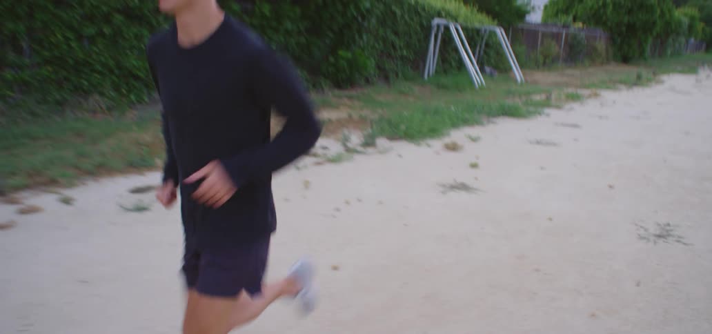 Man wearing white running shoes running shorts and black long sleeve t shirt jogs along a dirt road in the field