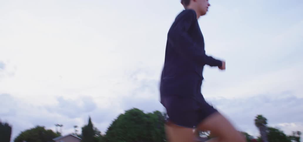 Man wearing black running shorts and white shoes runs down a road on a cloudy day