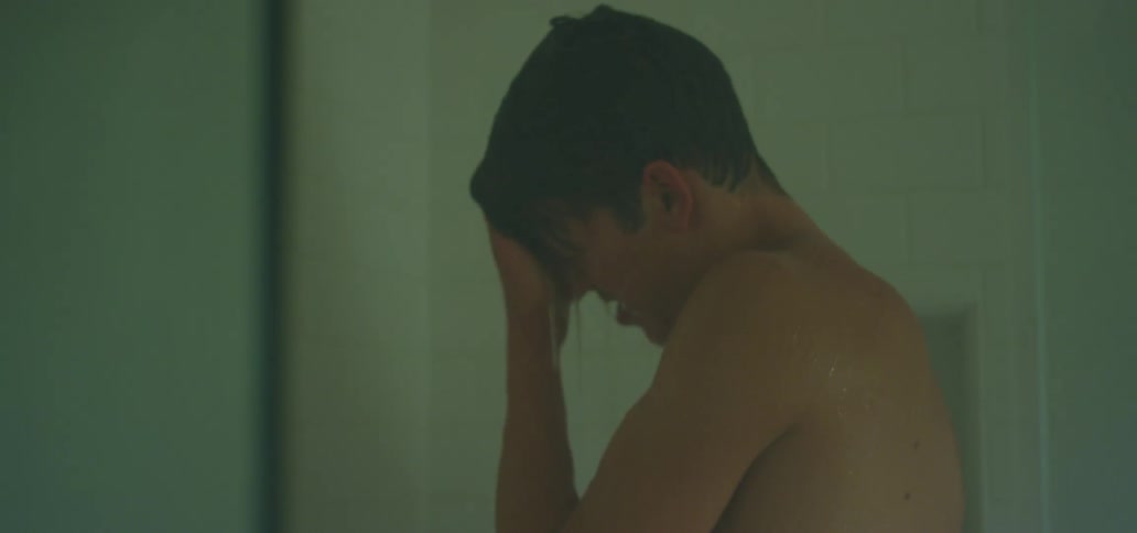 A teenager pushes his hair back as he showers in a locker room