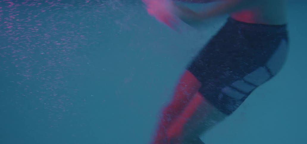 A young man does exercises in a pool before allowing himself to sink and running his hands through his hair
