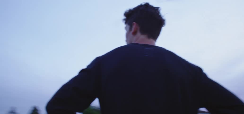 Young man wearing black sweater stands with hands on the hips outdoors in the morning