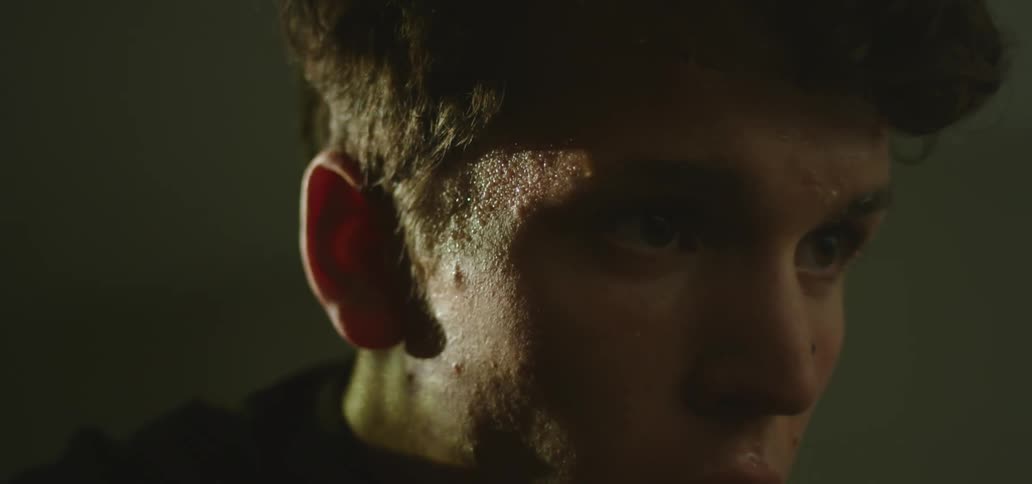 Close up of a young mans face swinging from side to side in a dimly lit room