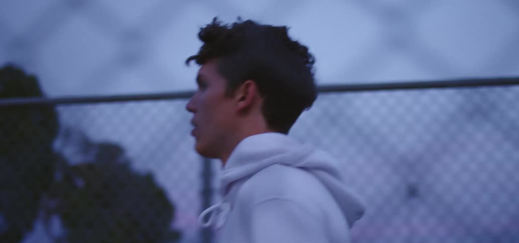 Young man wearing white hoodie walks between wired fences at morning