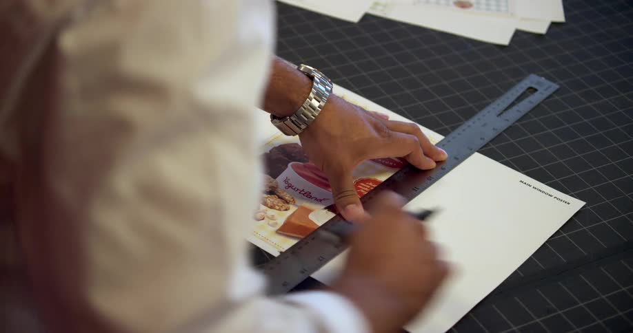 A man uses a ruler and a scalpel to cut off the blank areas of an advertisement