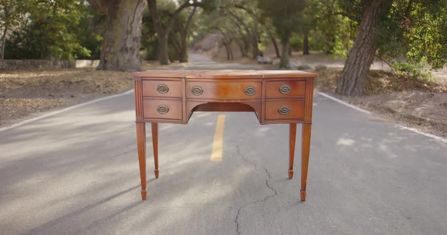 A dresser with drawers standing in the middle of the road with trees in the background