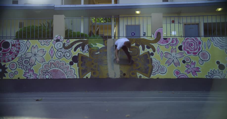 Young man jumps on a wall filled with graffiti street art in front of a house