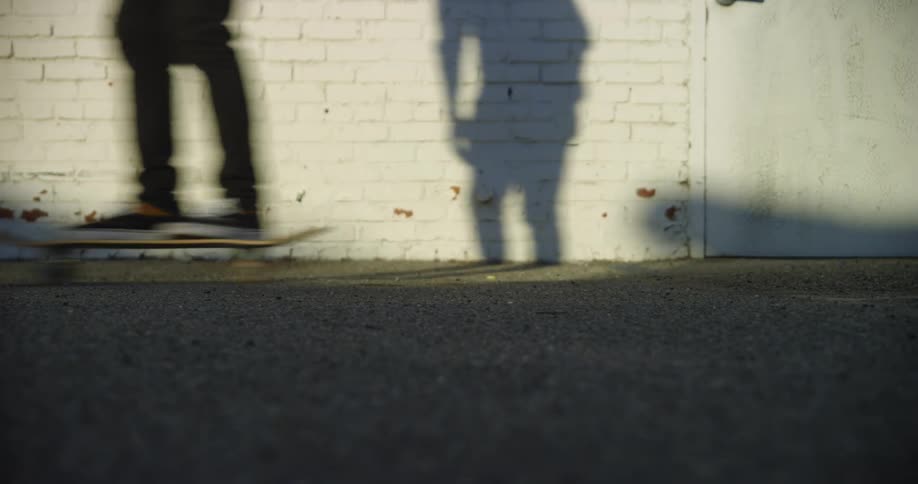 A skater glides effortlessly past a building with a white brick wall and a door