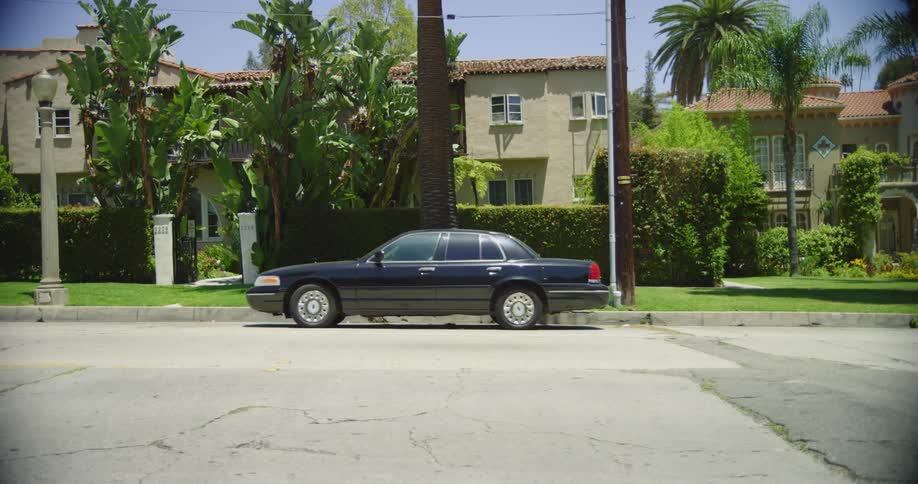 Blue sedan parked in front of a house in a neighborhood drives away