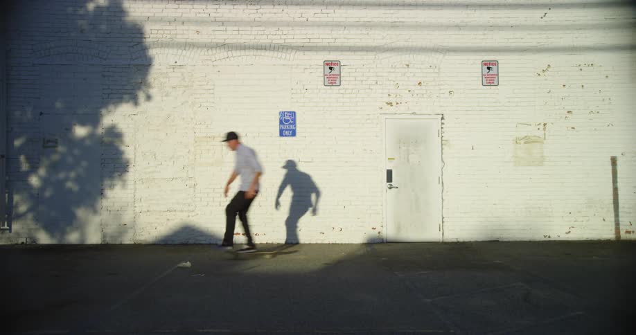 A man in a hat skating on a skateboard with a wall in the background