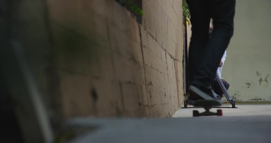 A camera operator uses a camera on a tripod to film a skateboarder skating towards him