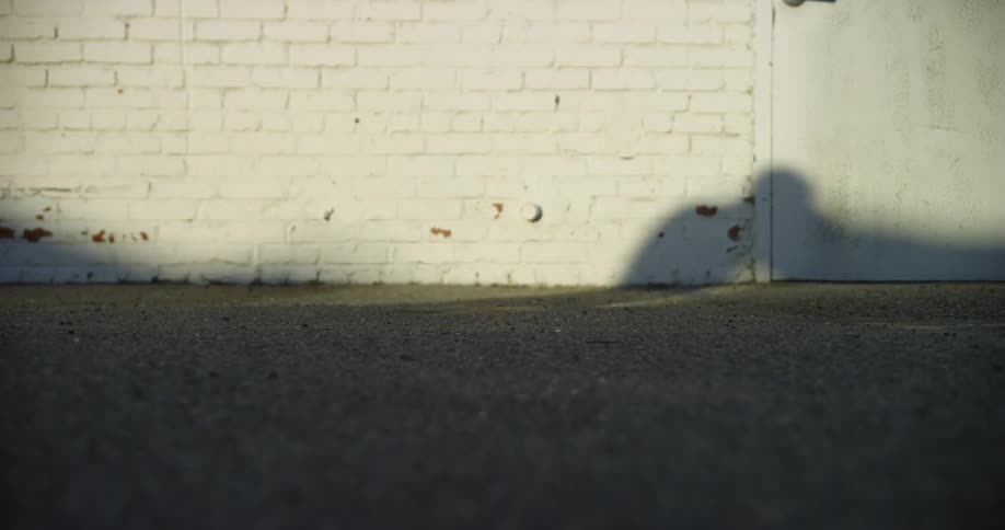 Shadow of a skater reflecting in the white brick wall of a building outdoors