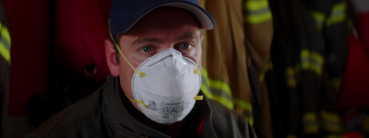 A firefighter is wearing a mask near a row of uniforms