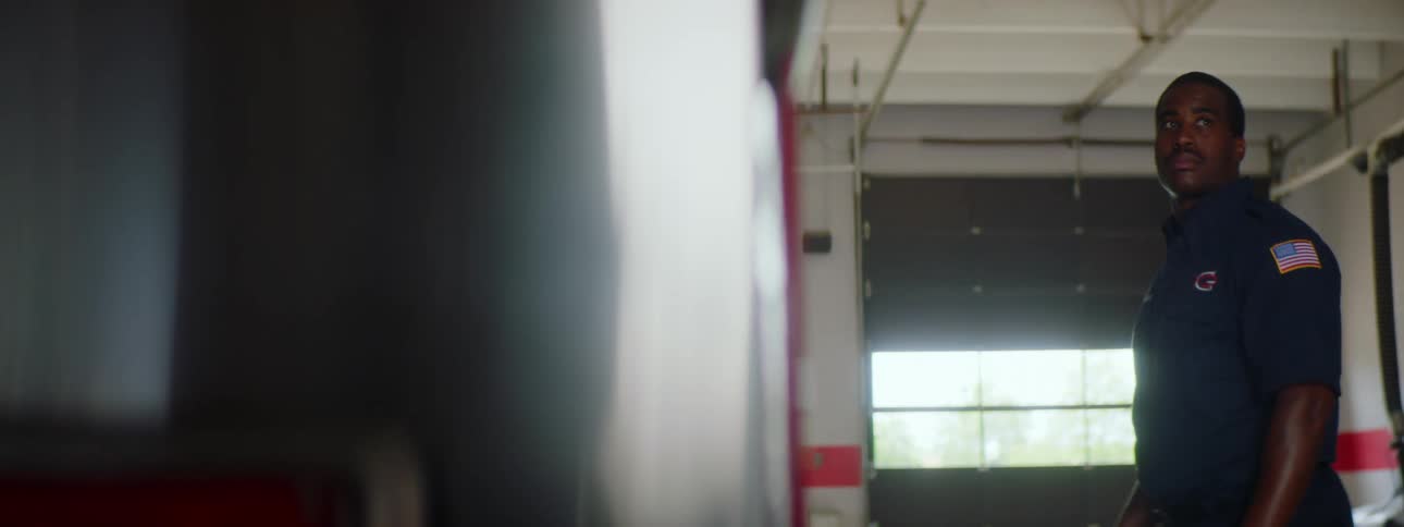 Male firefighter stands in the fire hall next to a fire truck