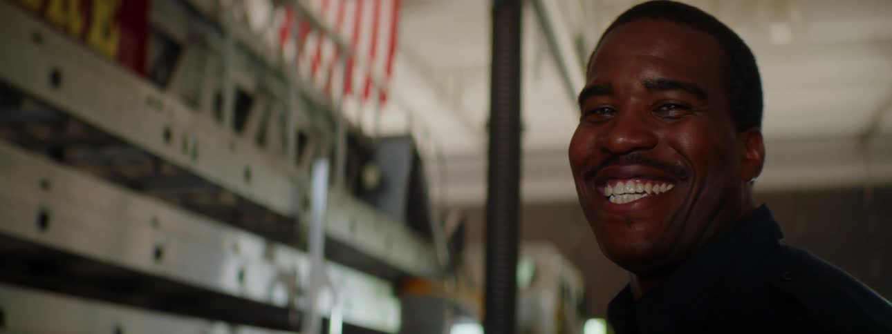 A firefighter smiles and laughs in a fire station