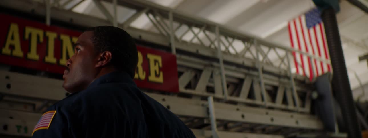Firefighter stands in front of a fire engine under an american flag inside a fire station