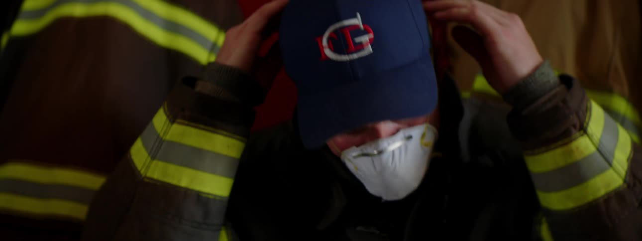 A firefighter sits on a bench in his uniform and puts on a dust mask