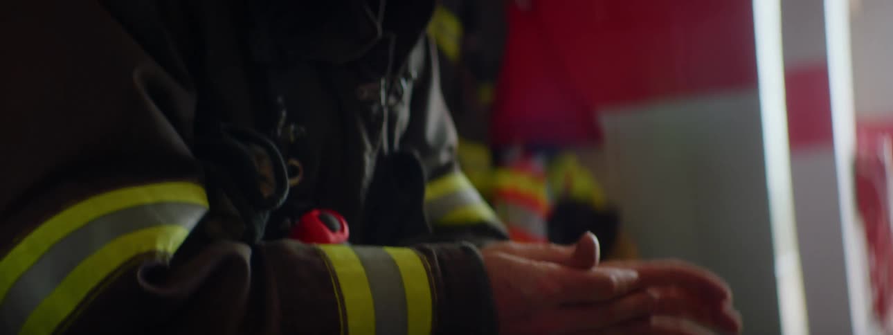 Firefighter wearing gear sits waiting rubbing his hands inside a fire station