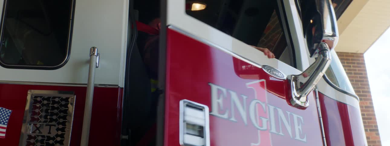 A firefighter closes the door of a fire engine as he puts on his seat belt
