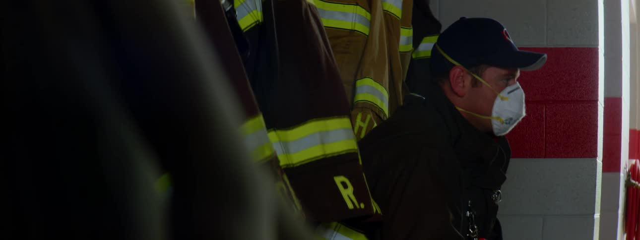 Firefighter with a cap and jacket sitting on a bench wears a white mask in the fire station