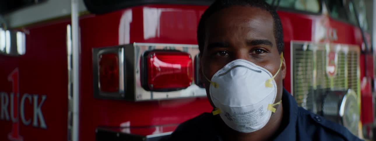 A firefighter wearing a mask stands in front of a fire truck