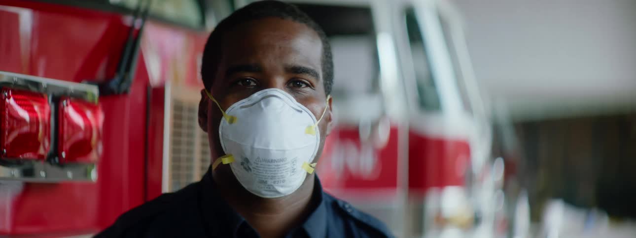 Man wearing a white face mask stands in front of emerency vehicles