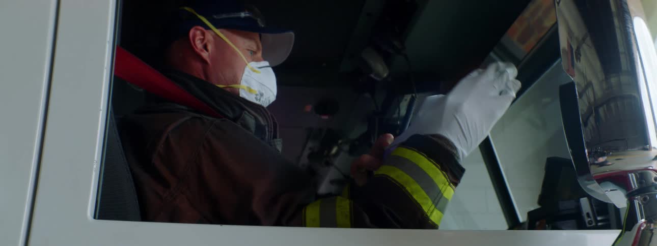 Firefighter wearing a mask puts on white latex gloves while sitting in the copilot seat of a firetruck