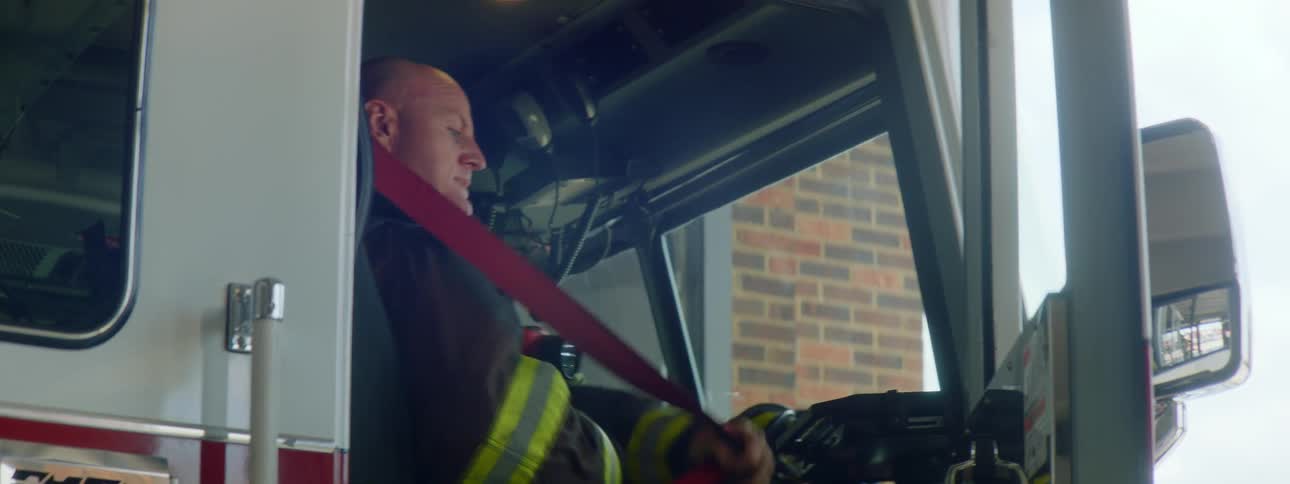 A fire fighter sitting in the passenger seat of a fire engine puts on his seatbelt as he closes the door
