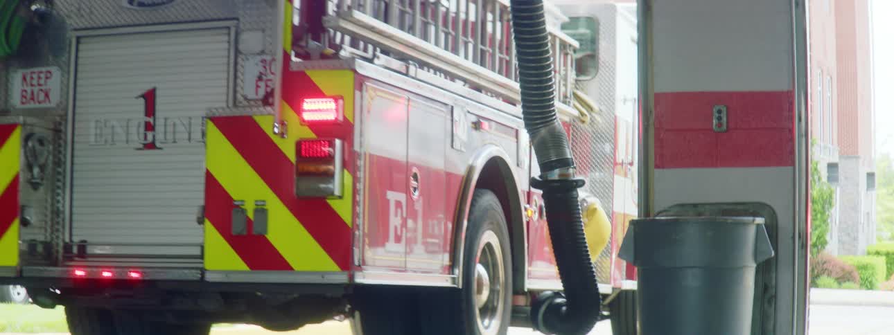 A fire engine pulls out of a fire station as a hose detaches itself from the vehicles side